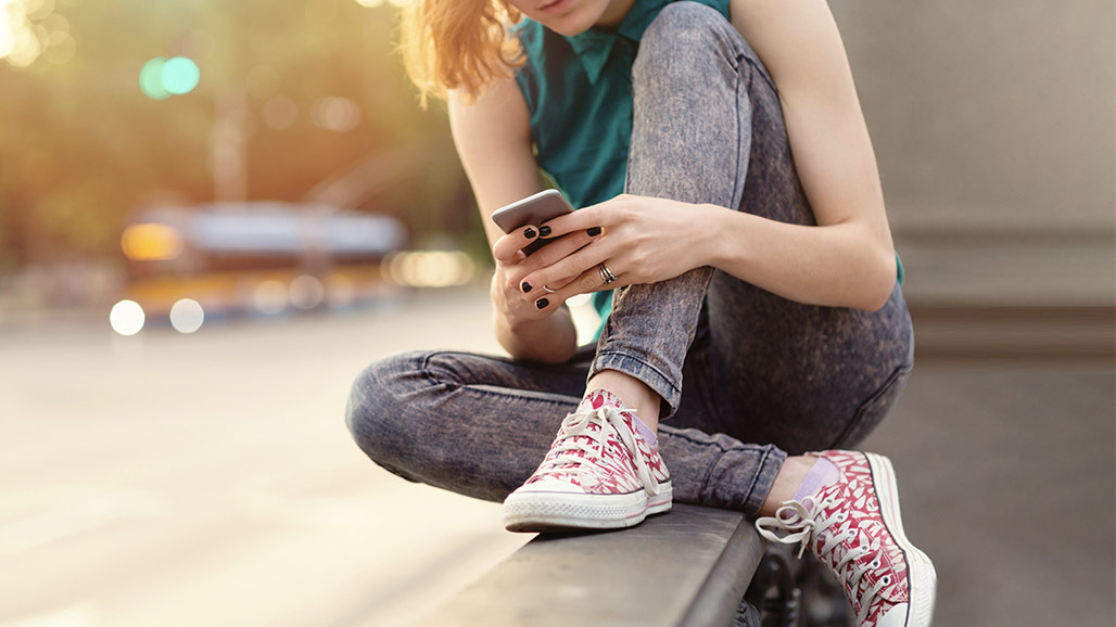 Cropped photo of teen sitting outside looking down at phone